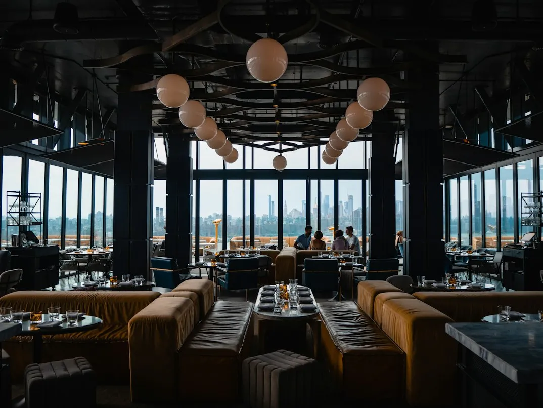 Rooftop hotel lounge with banquette seating and a city skyline through the windows