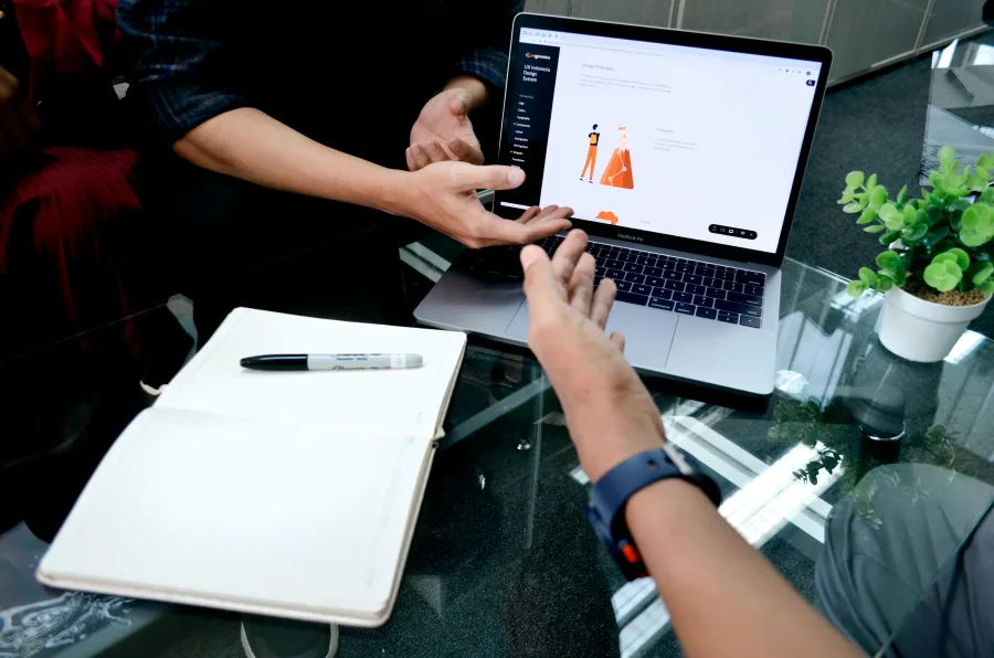 Two people working through documents on a laptop and an open notebook across a table